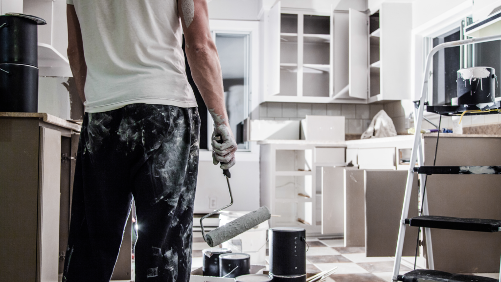 Person painting a white kitchen with a roller brush.